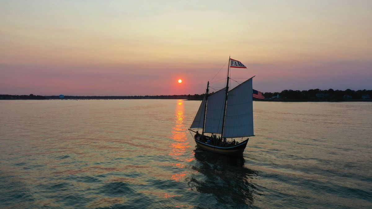 A sailboat is floating on top of a body of water at sunset.