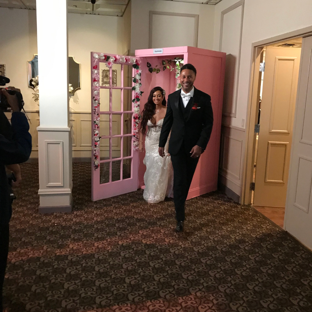 A bride and groom walk through a pink doorway