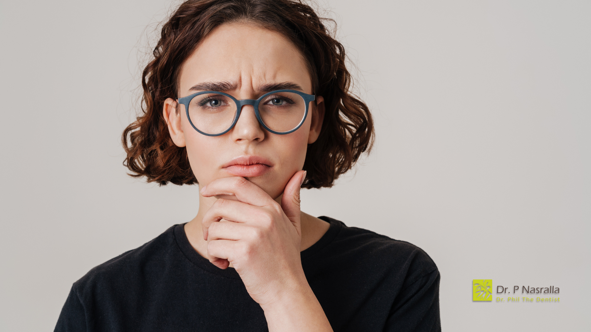 A woman wearing glasses is looking at the camera with her hand on her chin.