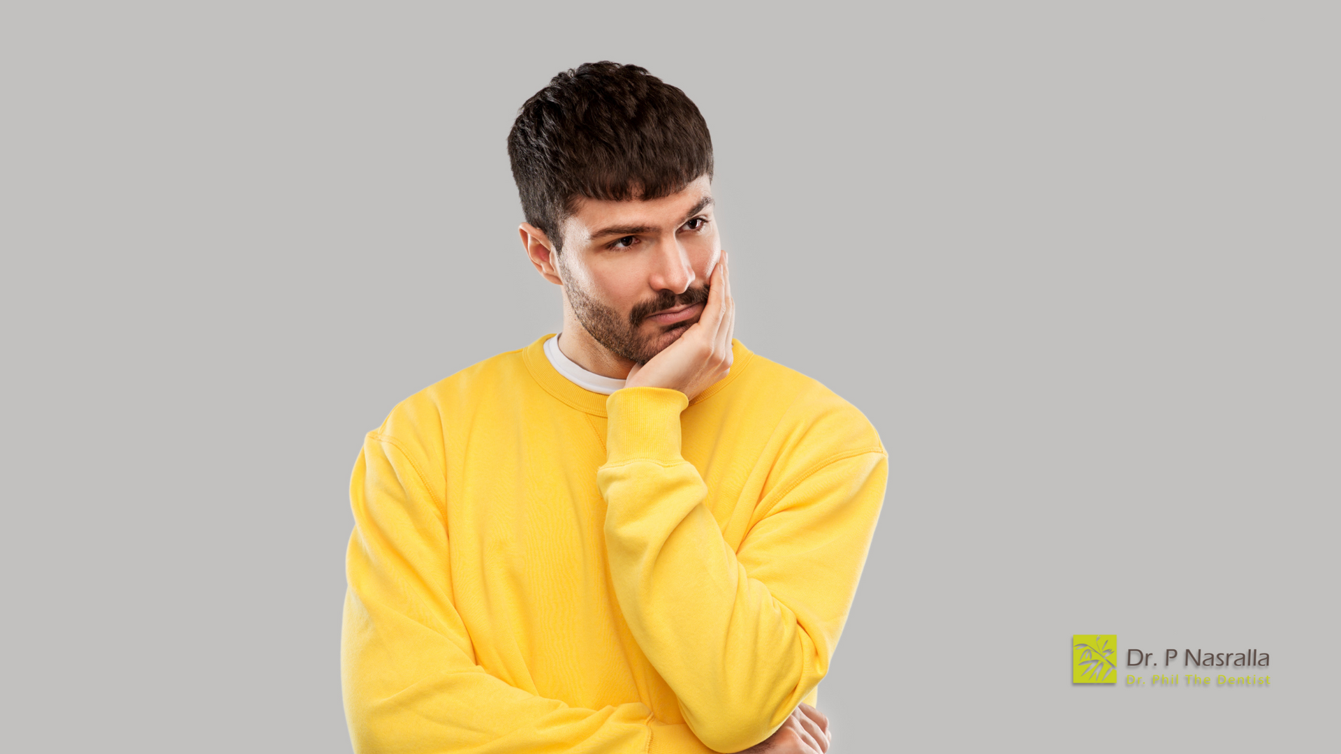 A man in a yellow sweater is thinking with his hand on his chin.