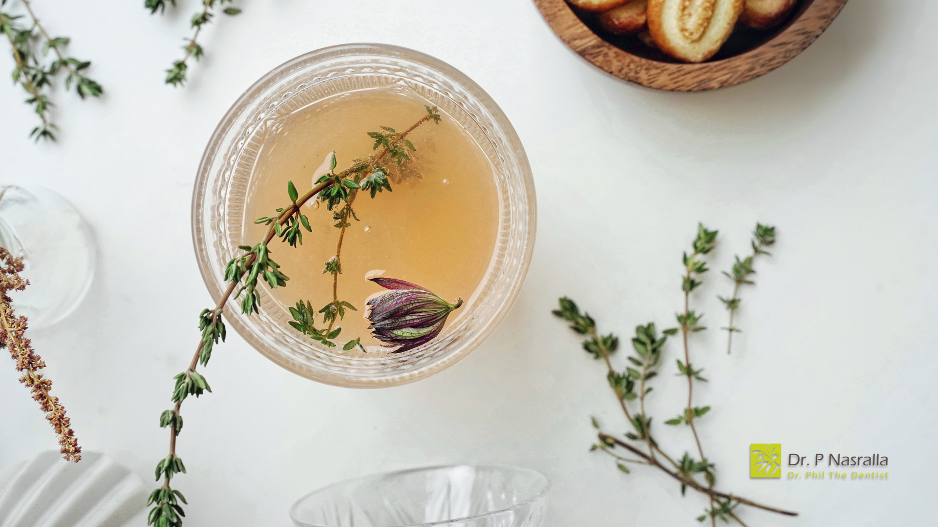 A glass of liquid with thyme leaves in it on a table.