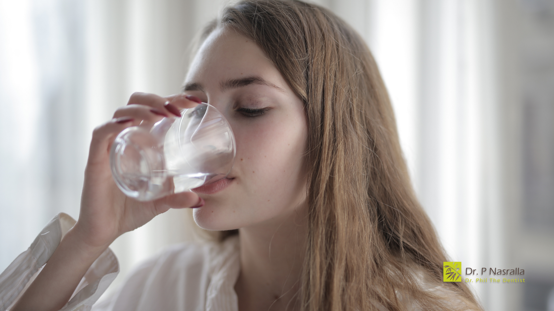 A woman is drinking water from a glass.