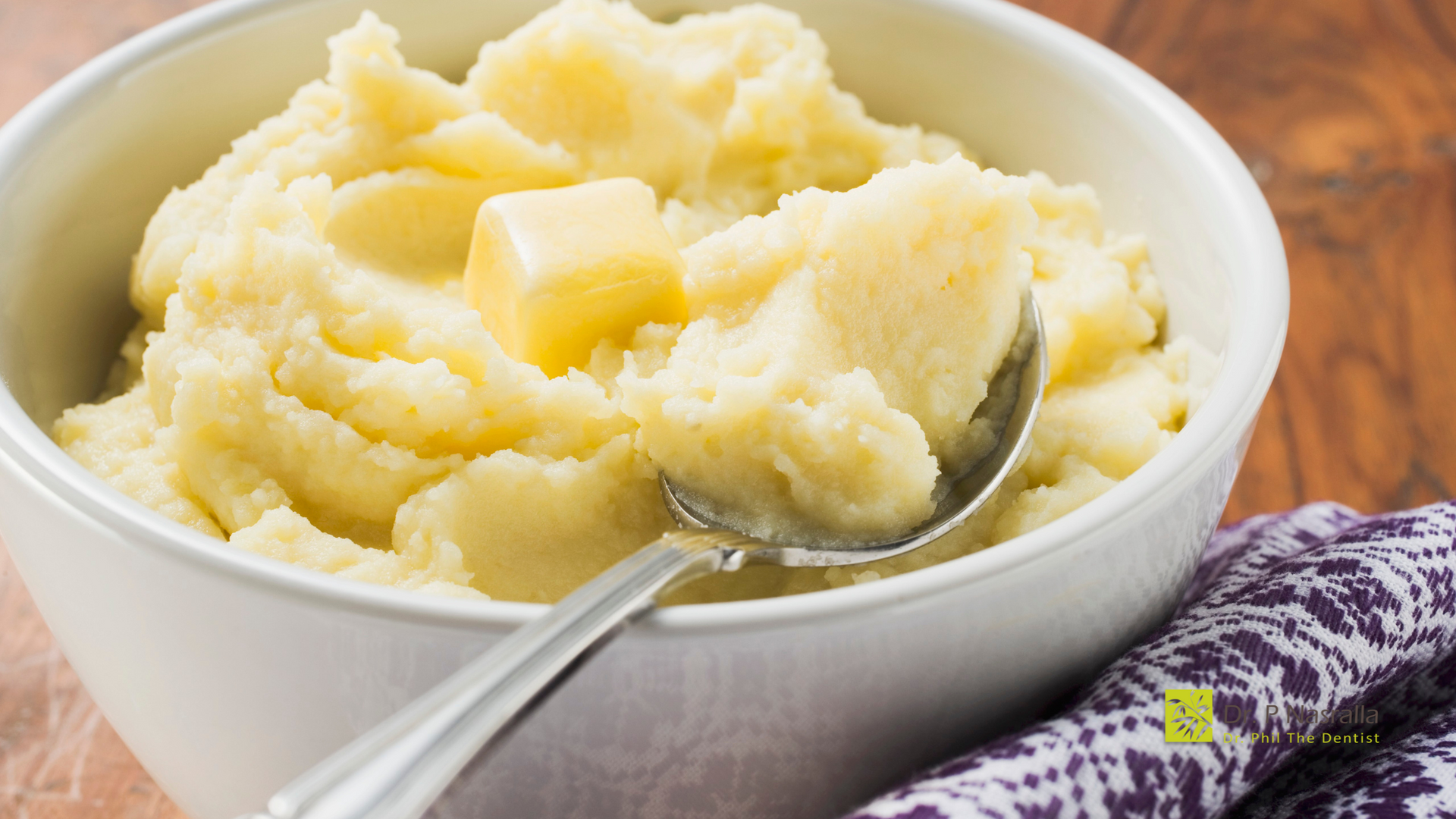 A bowl of mashed potatoes with butter and a spoon in it.