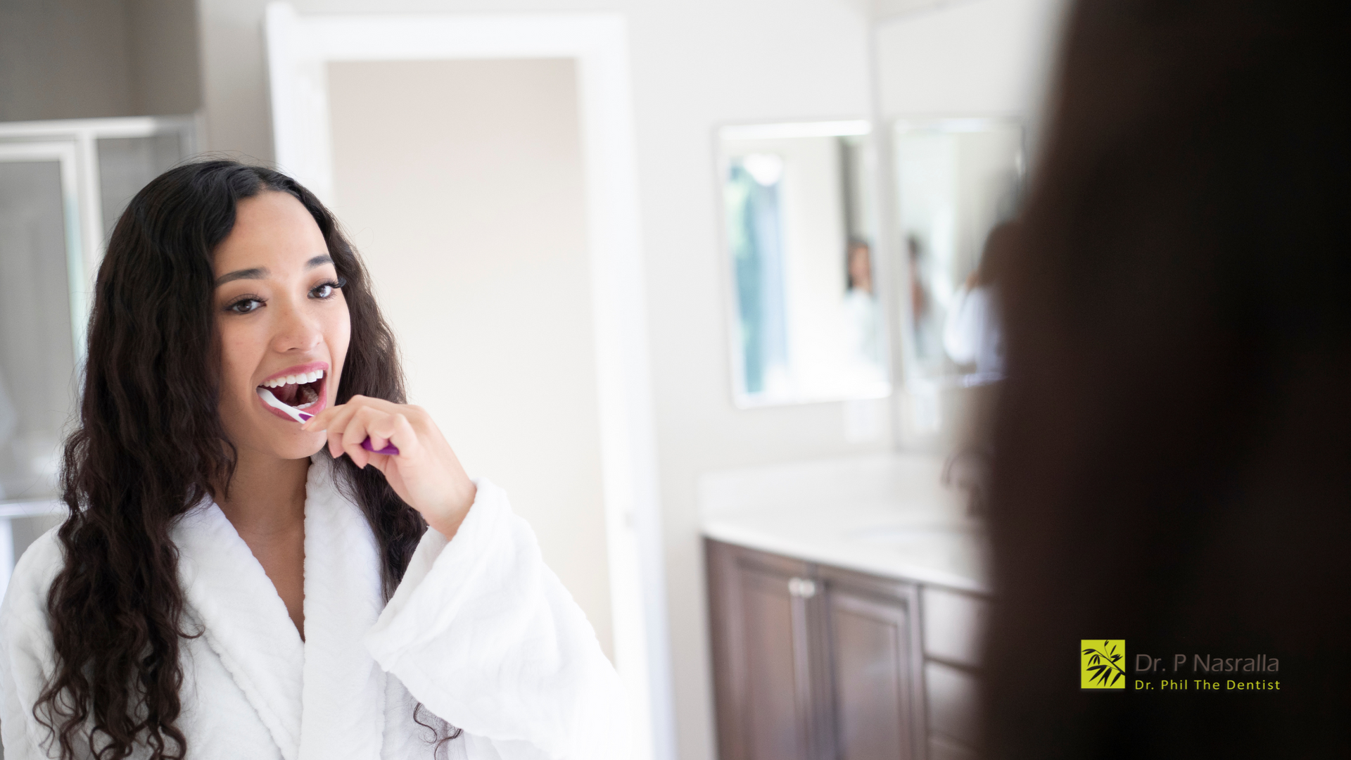 A woman is brushing her teeth in front of a mirror in a bathroom.
