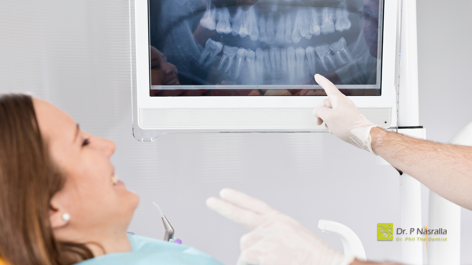 A woman is sitting in a dental chair looking at an x-ray of her teeth.