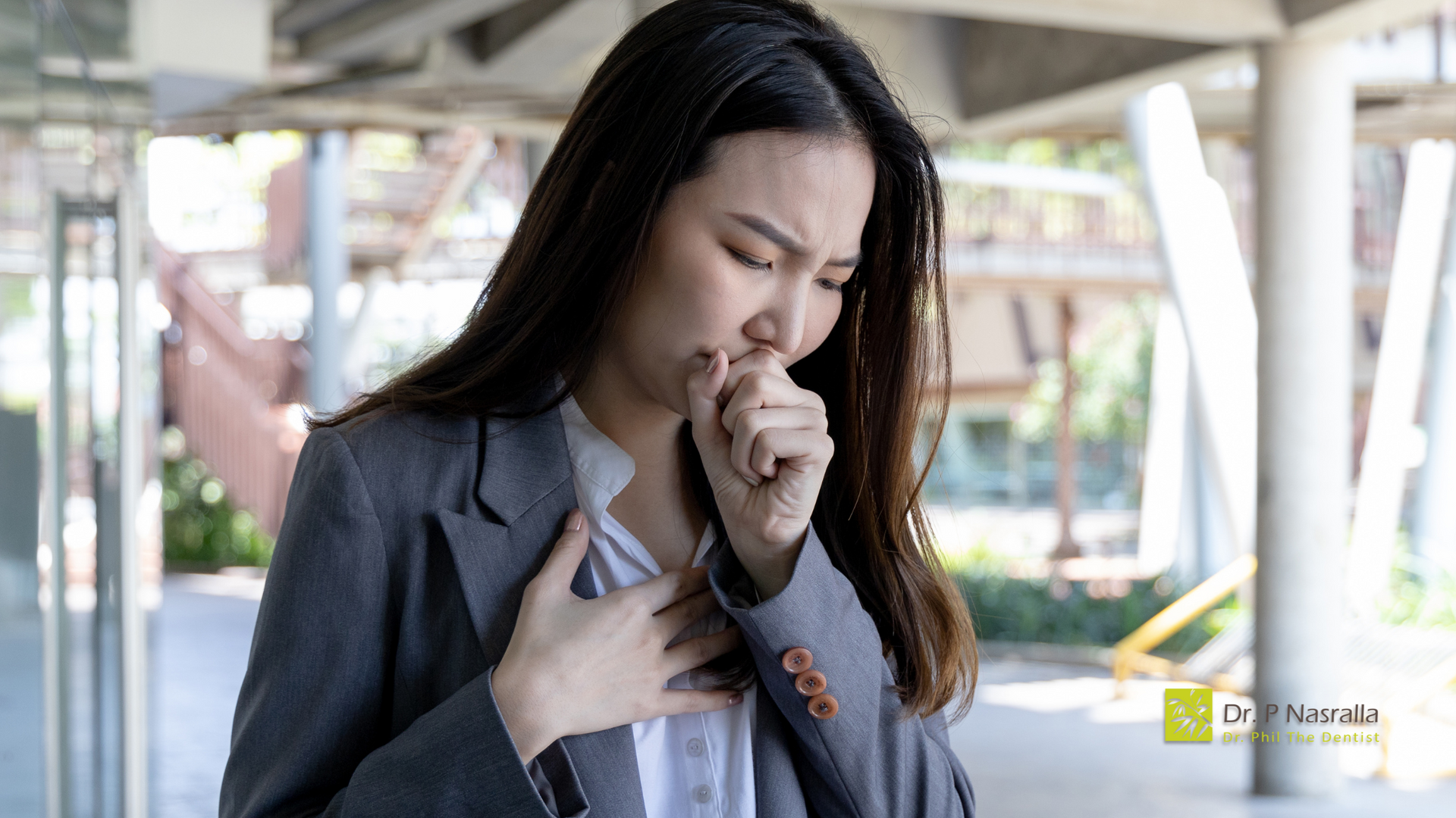 A woman in a suit is coughing while holding her chest.