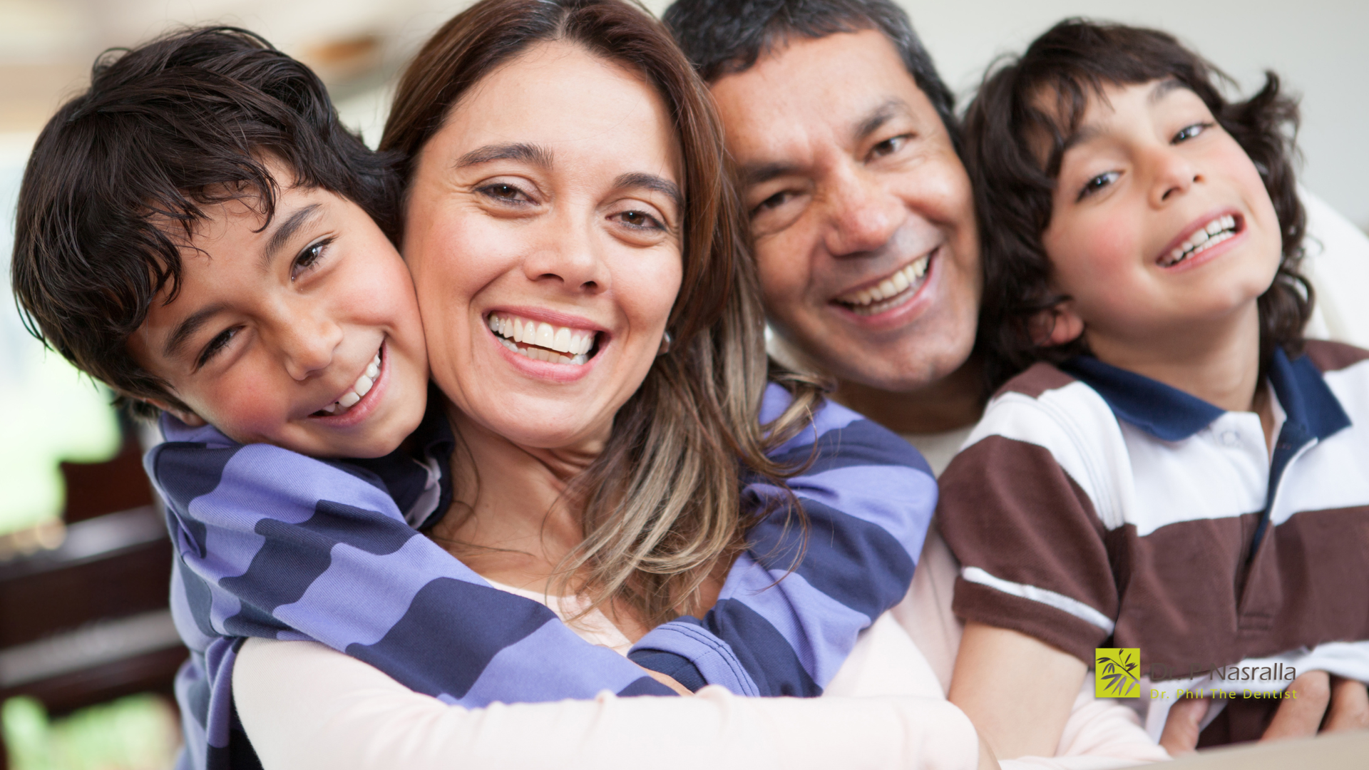Family of four smiling and embracing indoors.