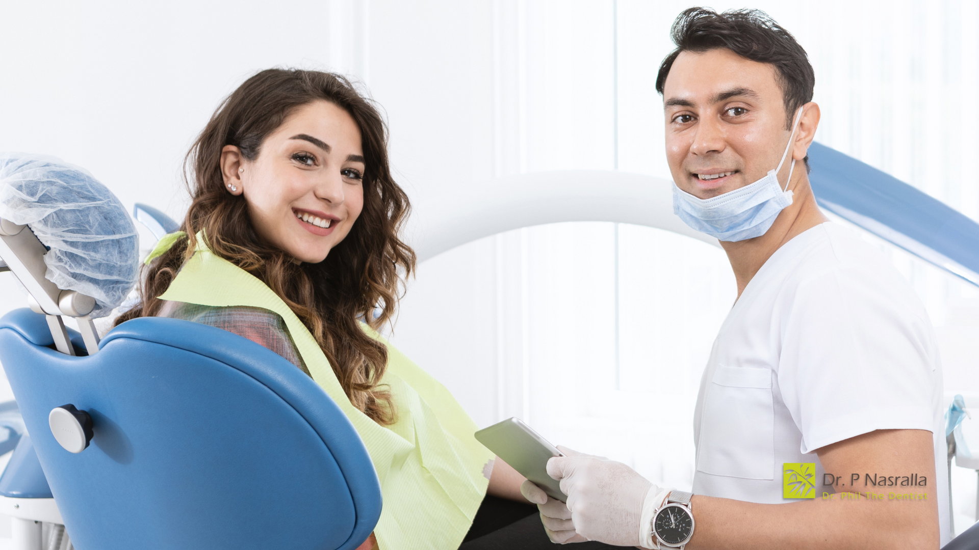 A woman is sitting in a dental chair next to a dentist.