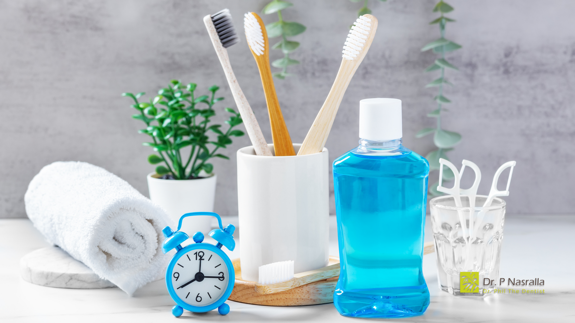 A bottle of mouthwash , toothbrushes , towels , and a clock on a table.