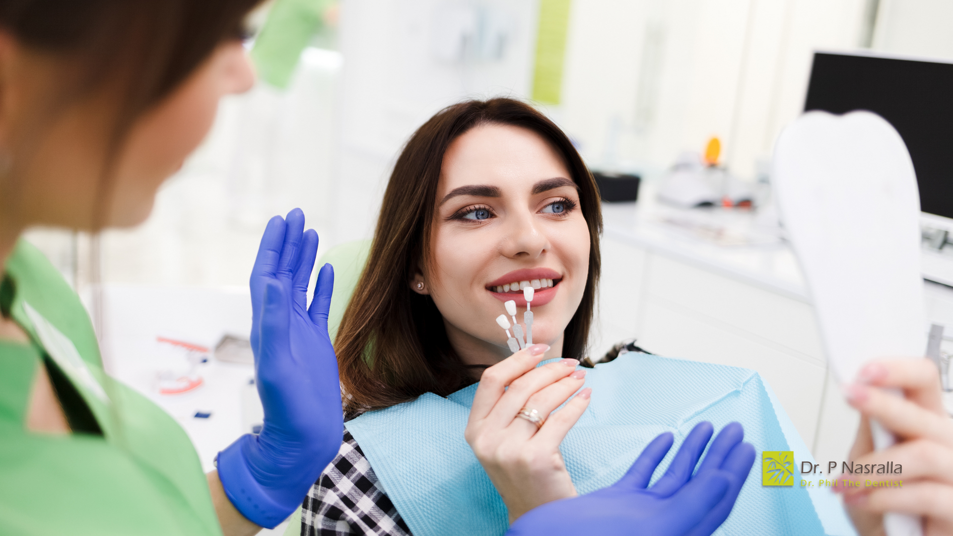 A woman is sitting in a dental chair looking at her teeth in a mirror.