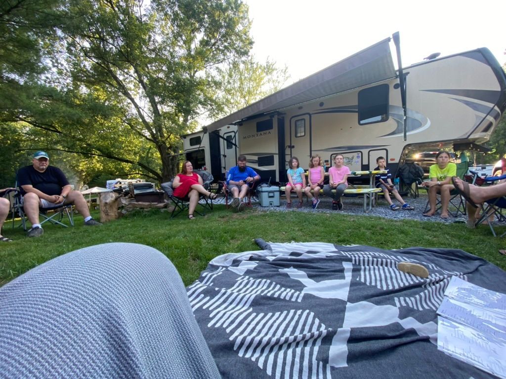 A group of people are sitting around a fire pit in front of a rv.