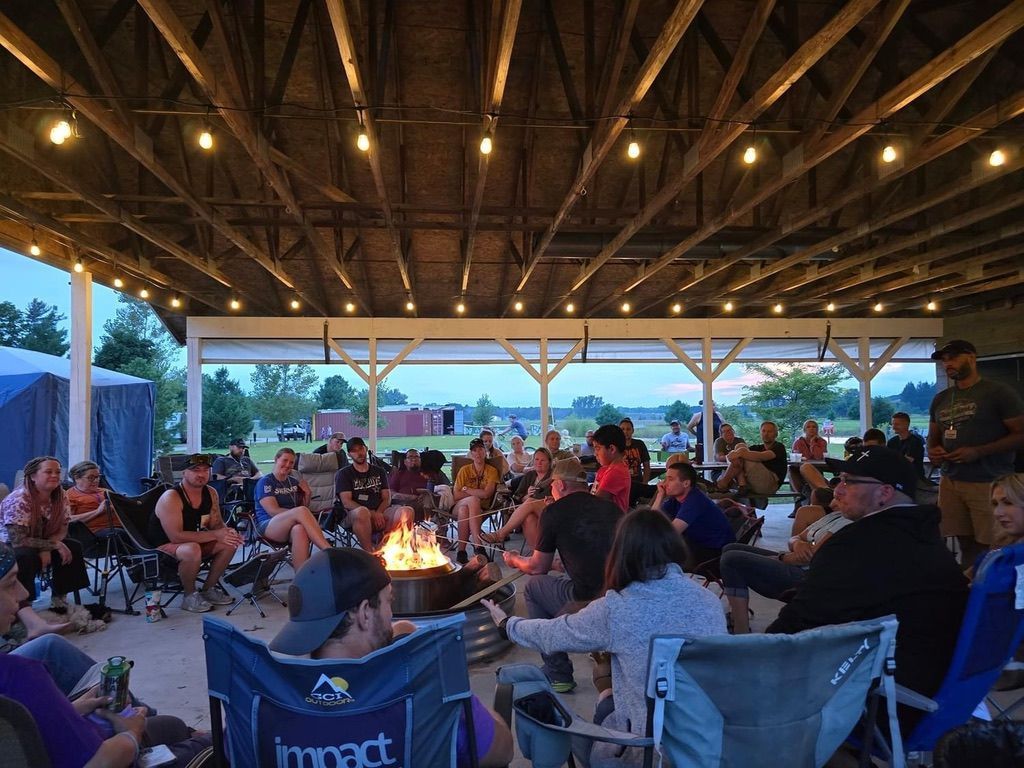 A group of people are sitting around a fire pit under a covered area.