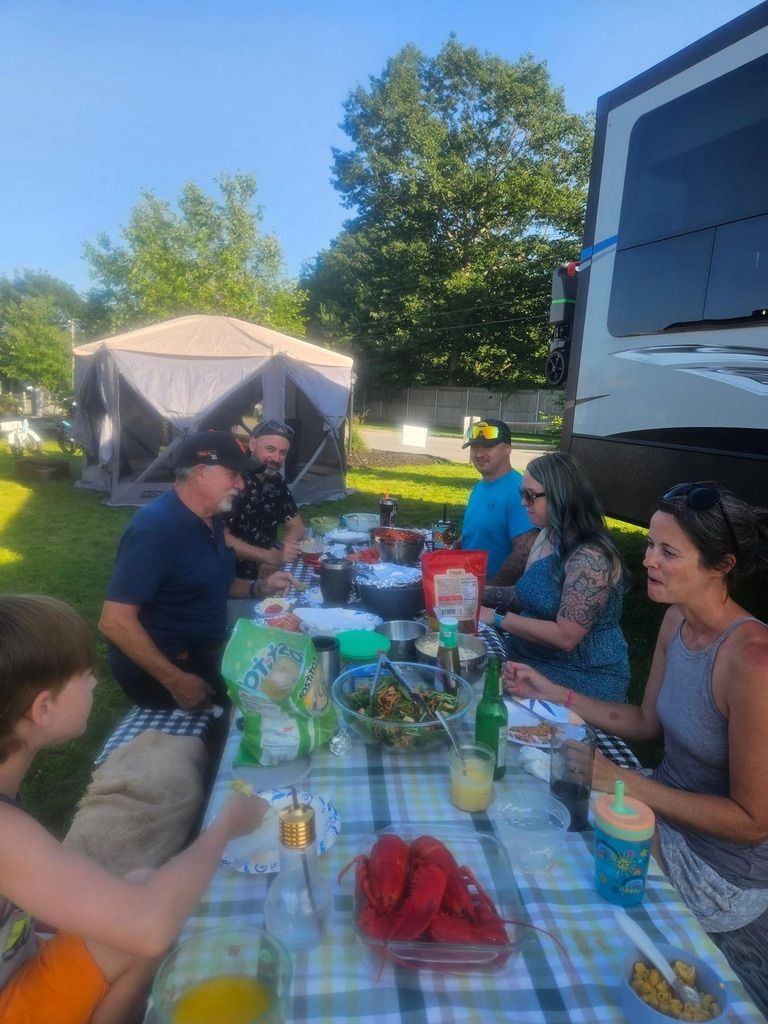 A group of people are sitting at a picnic table in front of a rv.