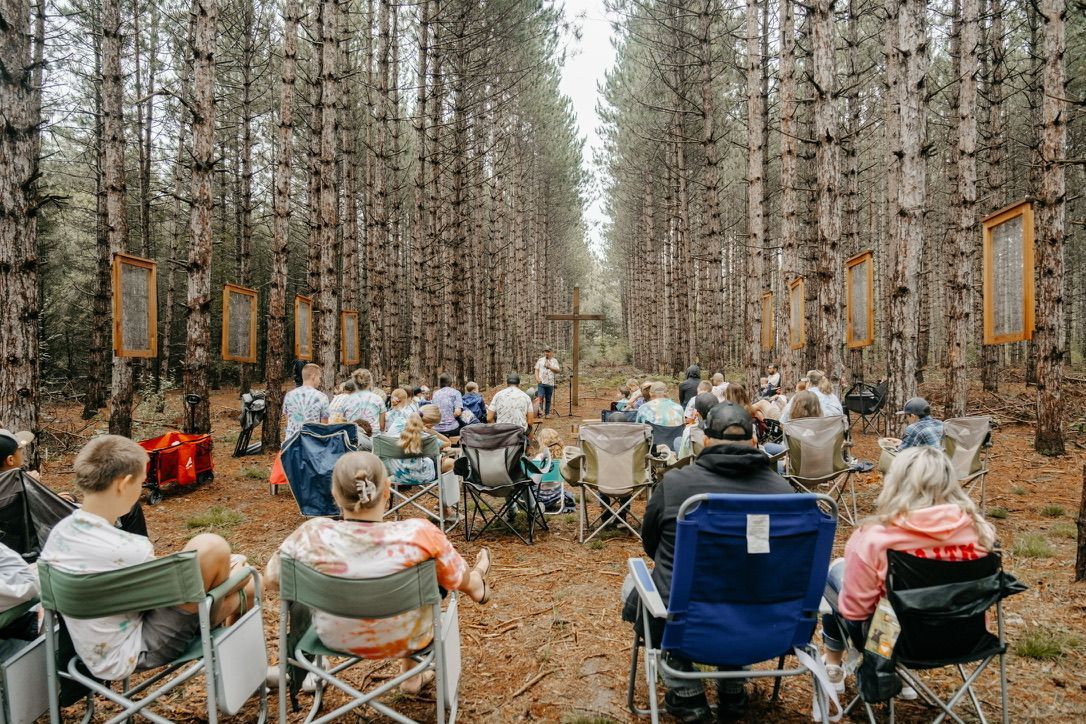 A group of people are sitting in folding chairs in the middle of a forest.
