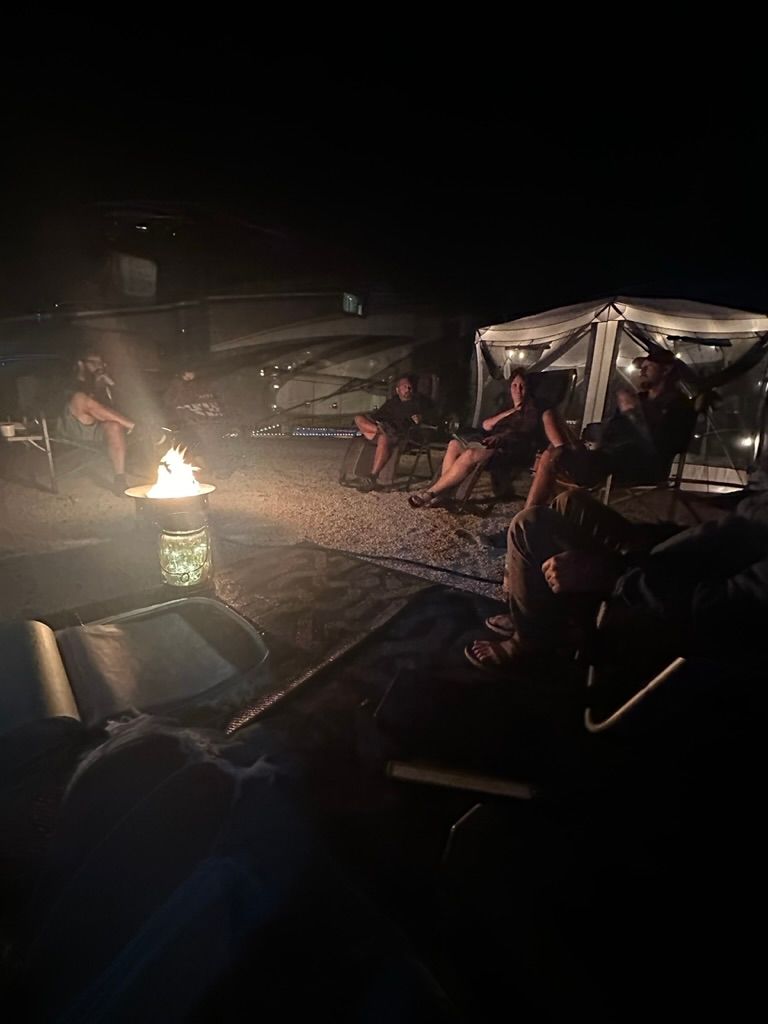 A group of people are sitting around a campfire at night.