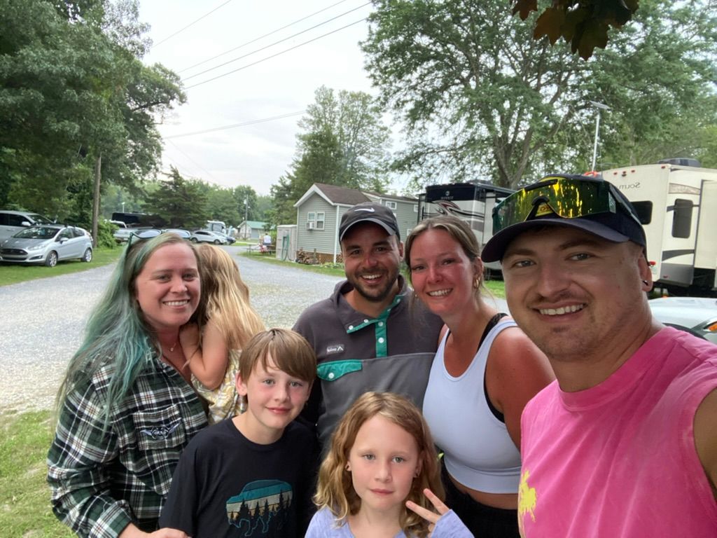 A group of people posing for a picture with a camper in the background