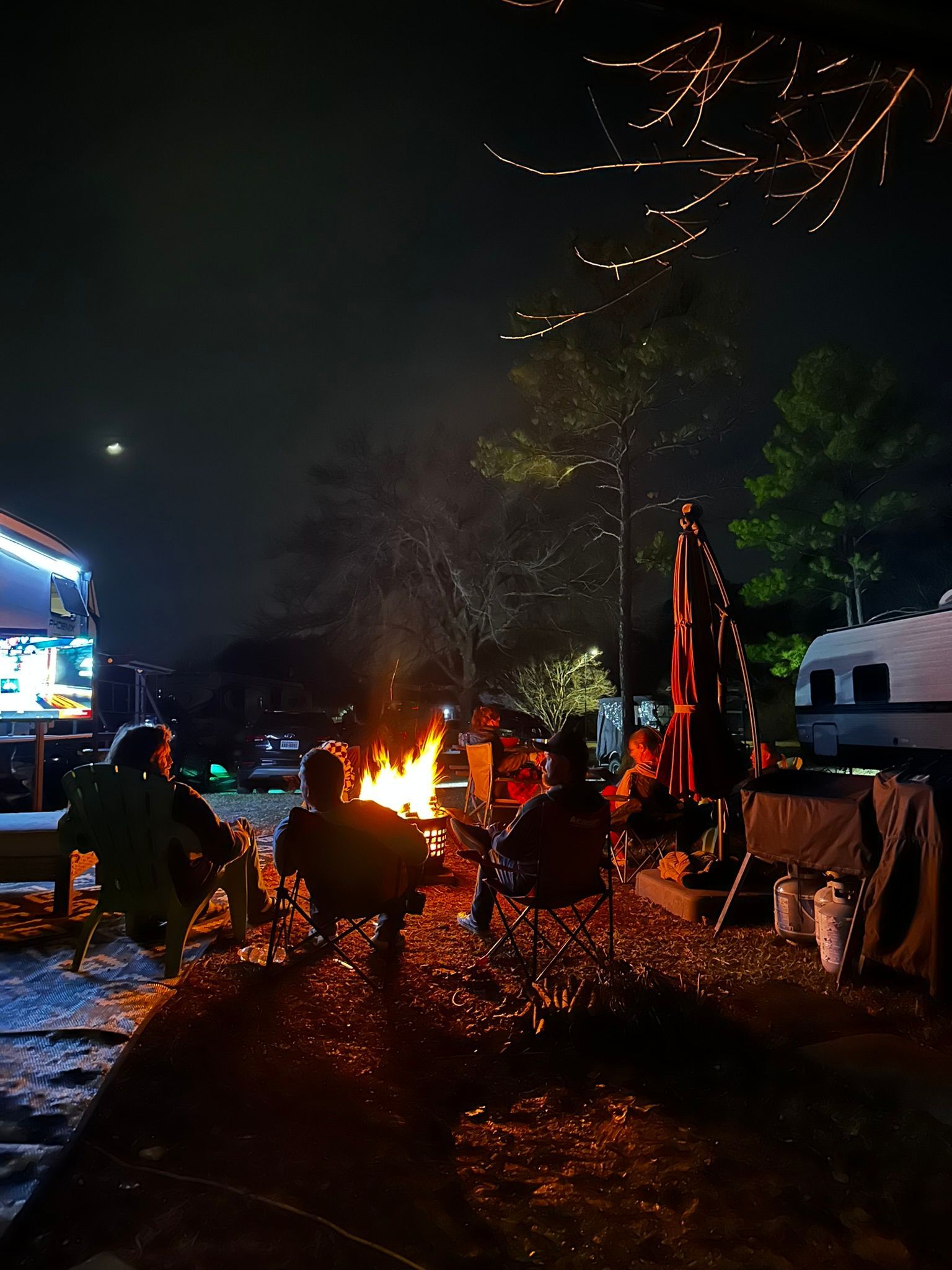 A group of people are sitting around a campfire at night.