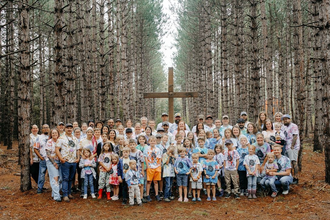 A large group of people are posing for a picture in the woods in front of a cross.