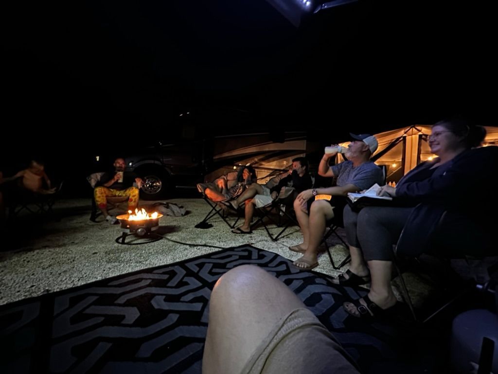 A group of people are sitting around a fire pit at night.