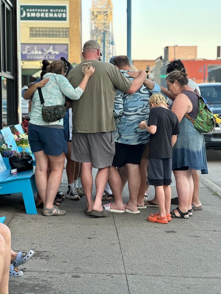 A group of people are praying on the sidewalk in front of a store called lake ave
