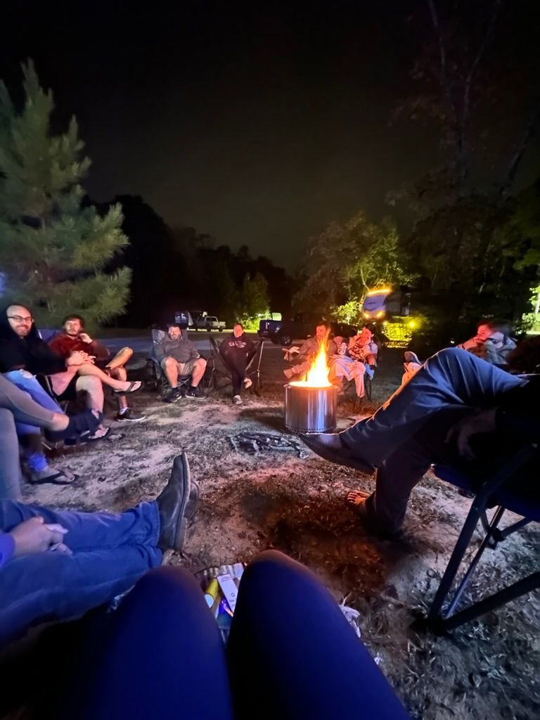 A group of people are sitting around a campfire at night.