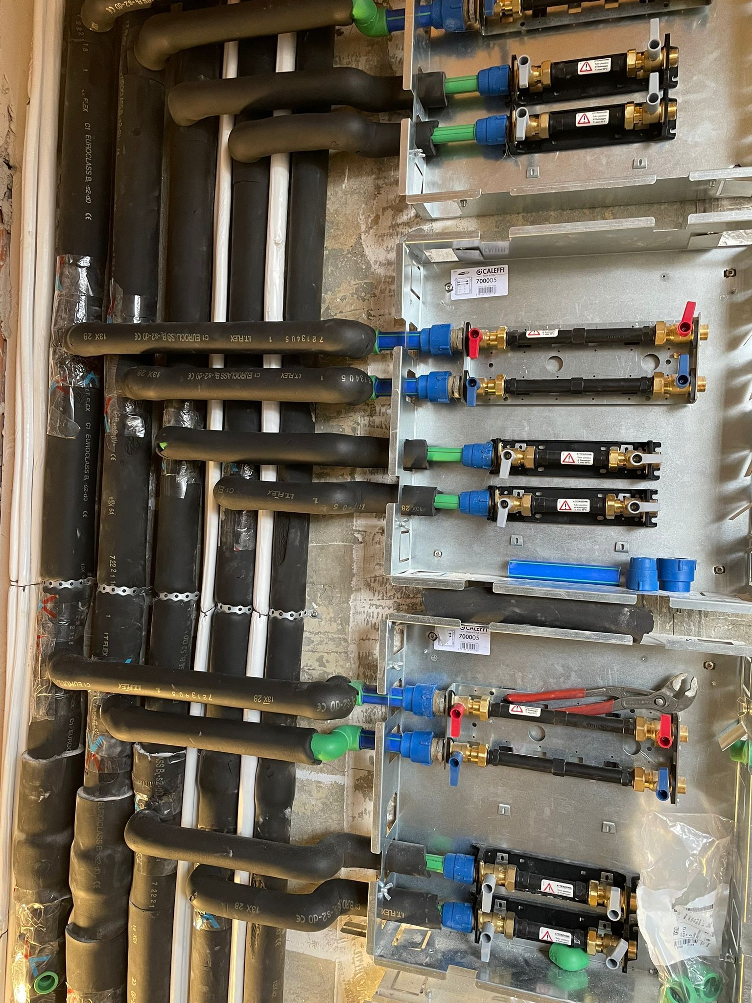 Tubi con isolamento e raccordi blu e rossi. Installazione a parete.