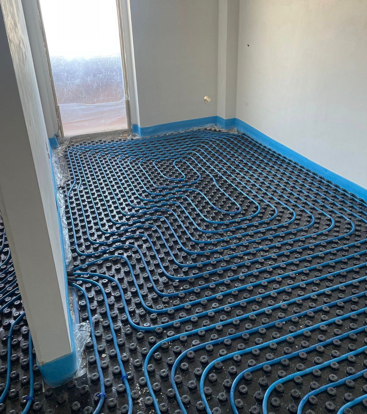 Tubi rossi che formano la griglia del sistema di riscaldamento a pavimento su un pavimento in una stanza in costruzione.