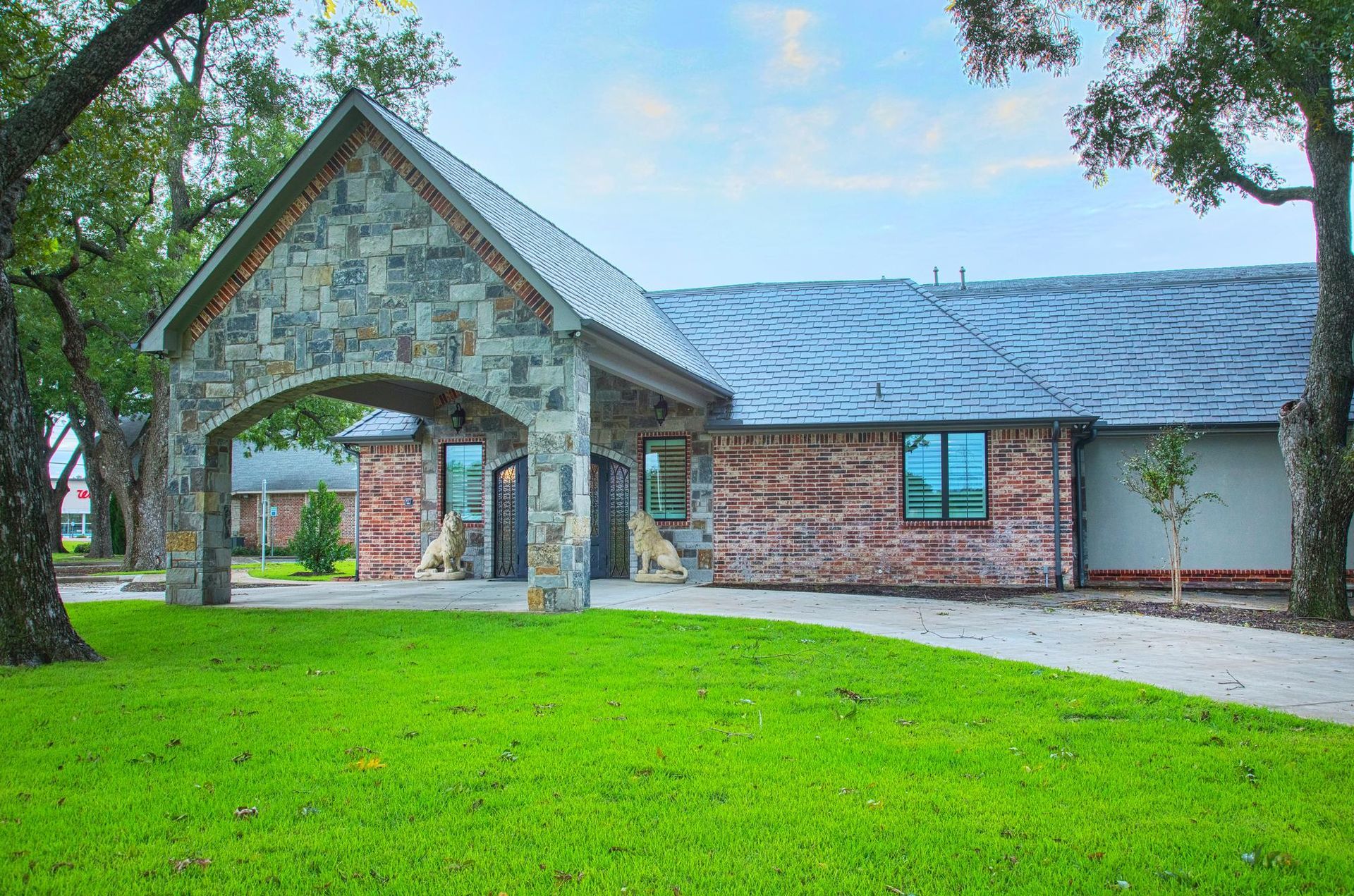 A large brick house with a stone archway and a lush green lawn in front of it.