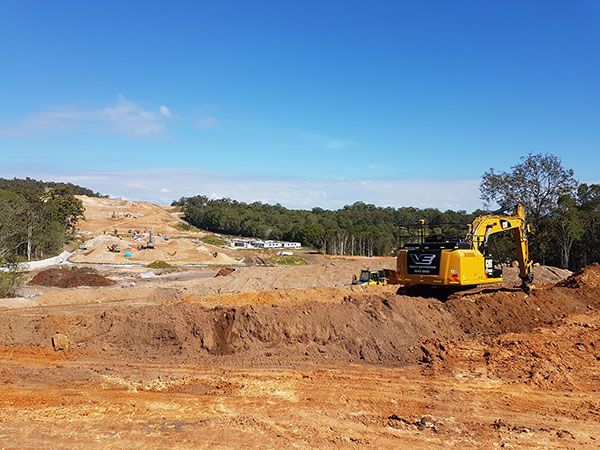 A yellow excavator is digging a hole in a dirt field.