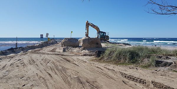 A large excavator is working on a beach next to the ocean.