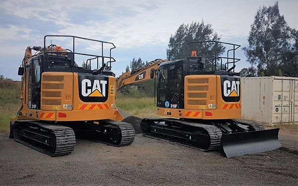 Two cat excavators are parked next to each other in a parking lot.