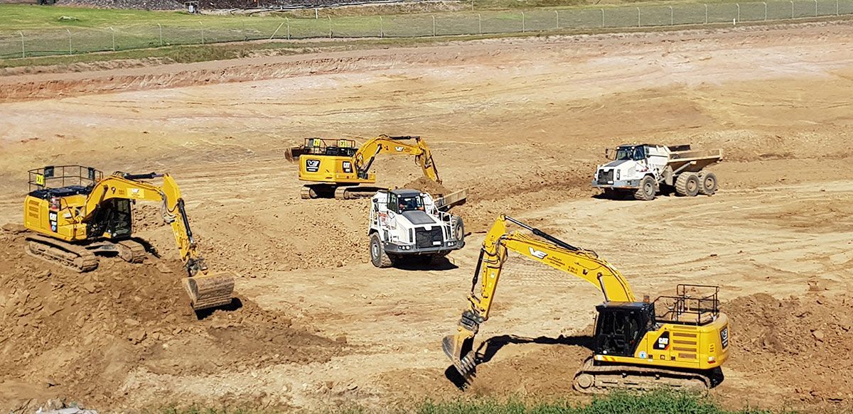 A group of construction vehicles are working on a dirt field.