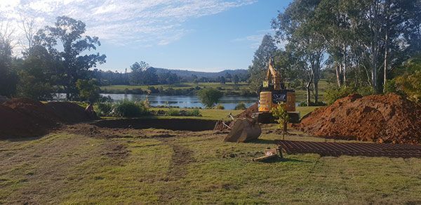 A bulldozer is digging a hole in a field next to a lake.