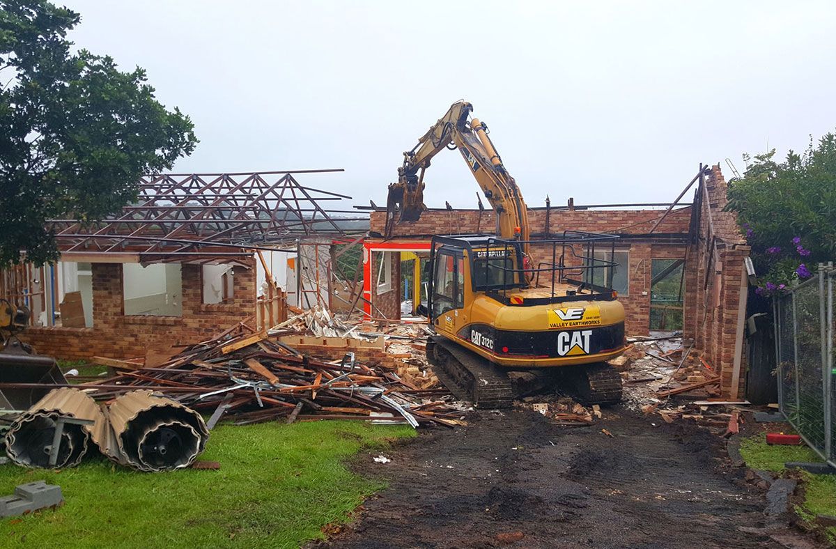 A cat excavator is demolishing a brick house.