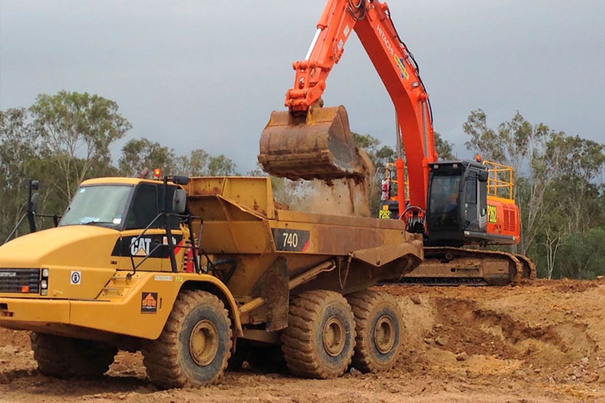 A cat dump truck is being loaded with dirt by an excavator.
