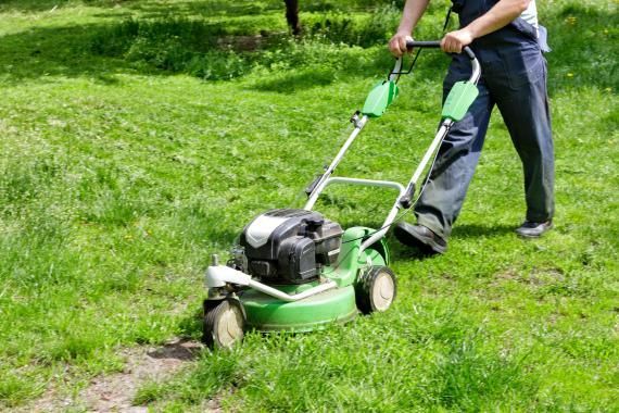 Un homme utilise une tondeuse à gazon verte pour couper l'herbe.