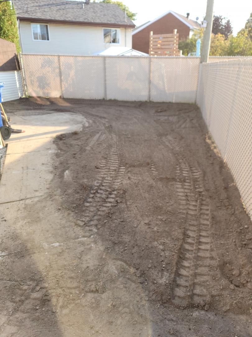 Un chemin de terre avec une clôture à mailles losangées et une maison en arrière-plan