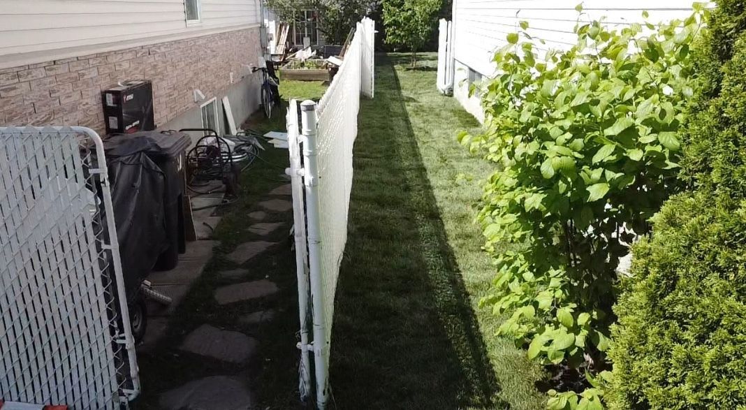 Une clôture blanche entoure une cour verdoyante à côté d’une maison.