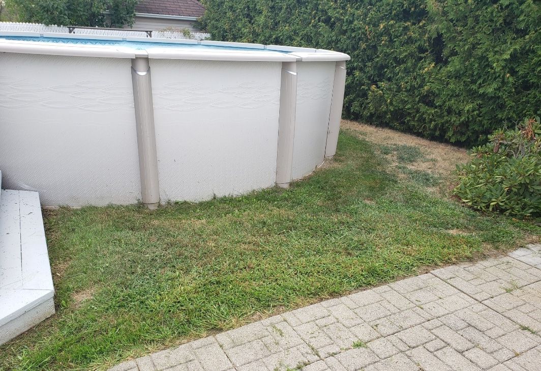 Une piscine blanche se trouve dans l’herbe à côté d’une passerelle en brique.