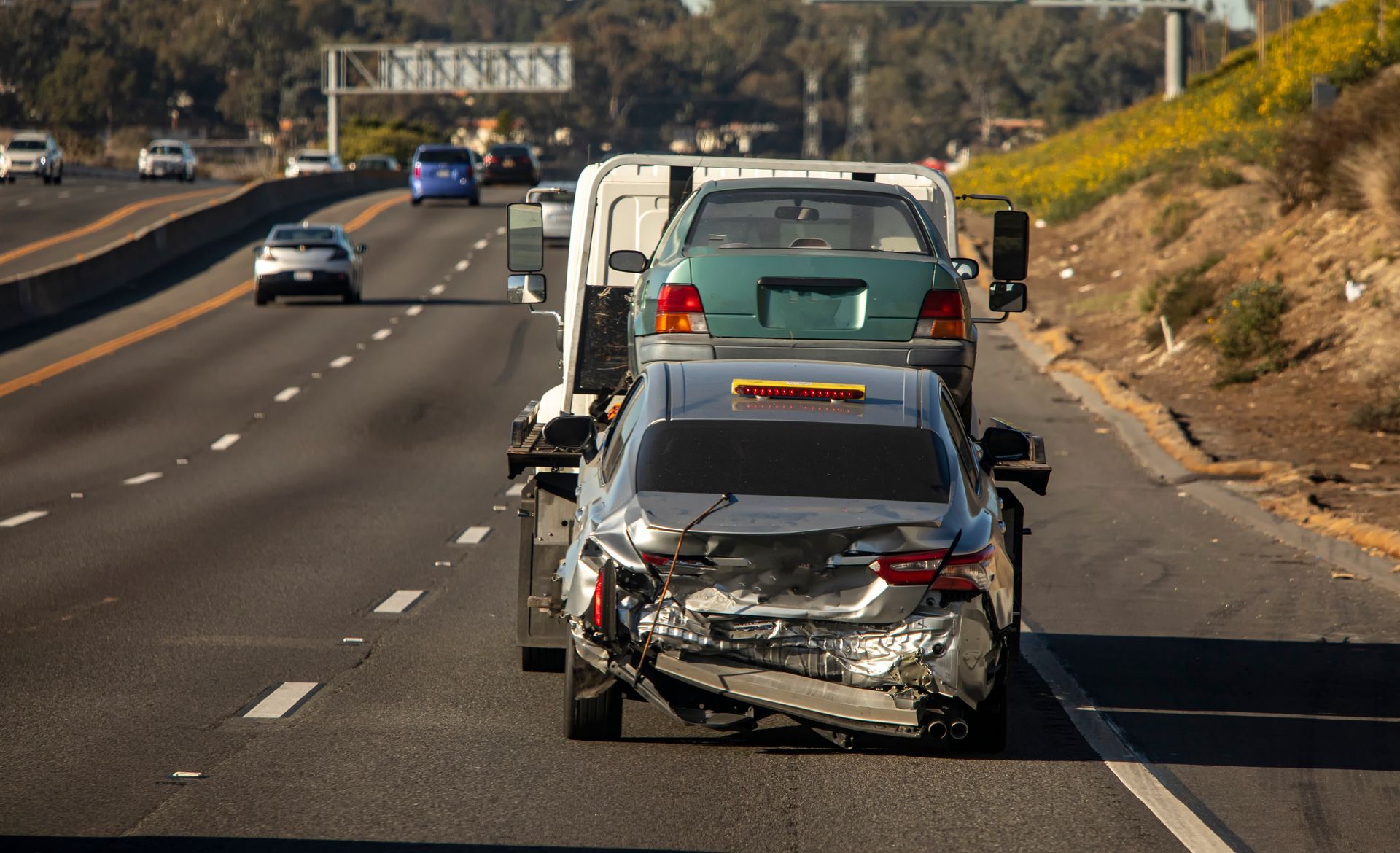 A tow truck is towing a damaged car on a highway.