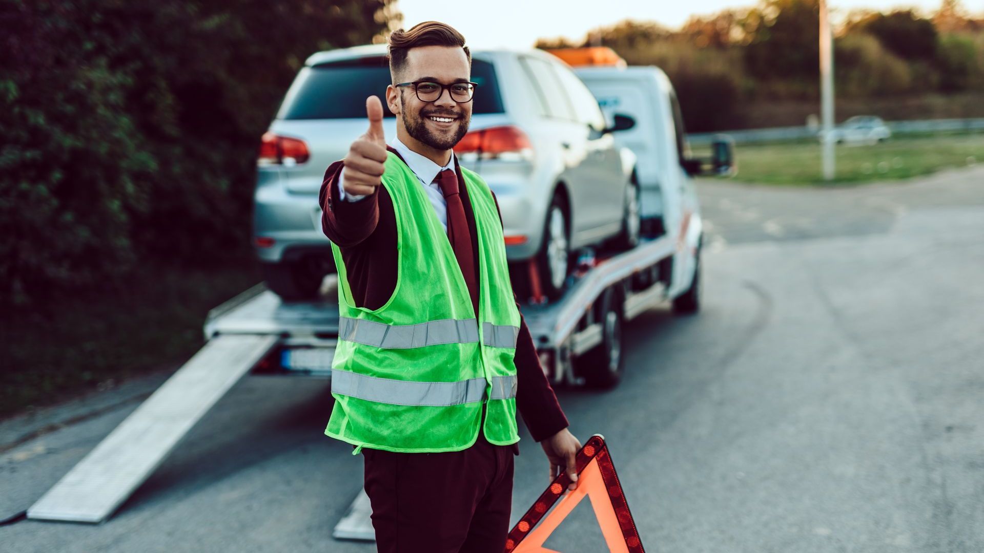 A man is giving a thumbs up in front of a tow truck.