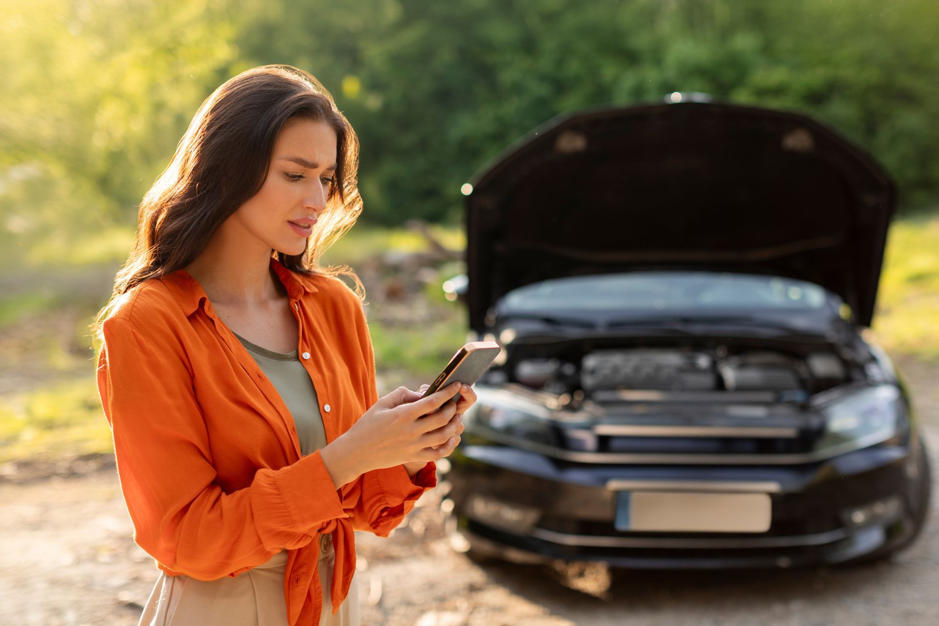 A woman is using a cell phone in front of a broken down car.