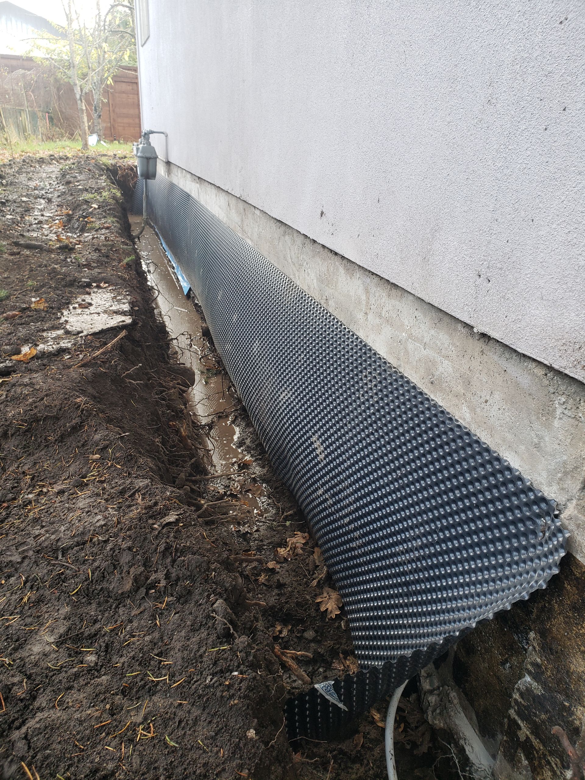 Drain cloth laid over freshly installed perimeter drain system in trench around home foundation