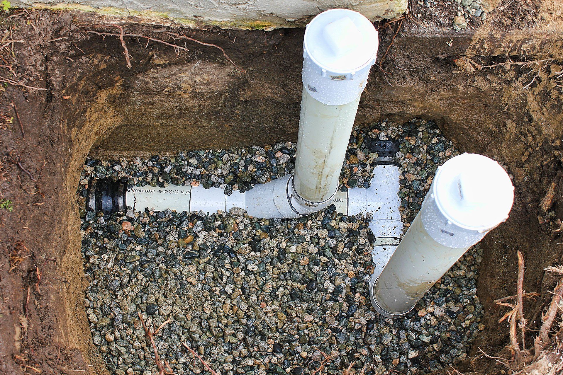 Newly installed drain pipes in an open trench with loose gravel at the bottom