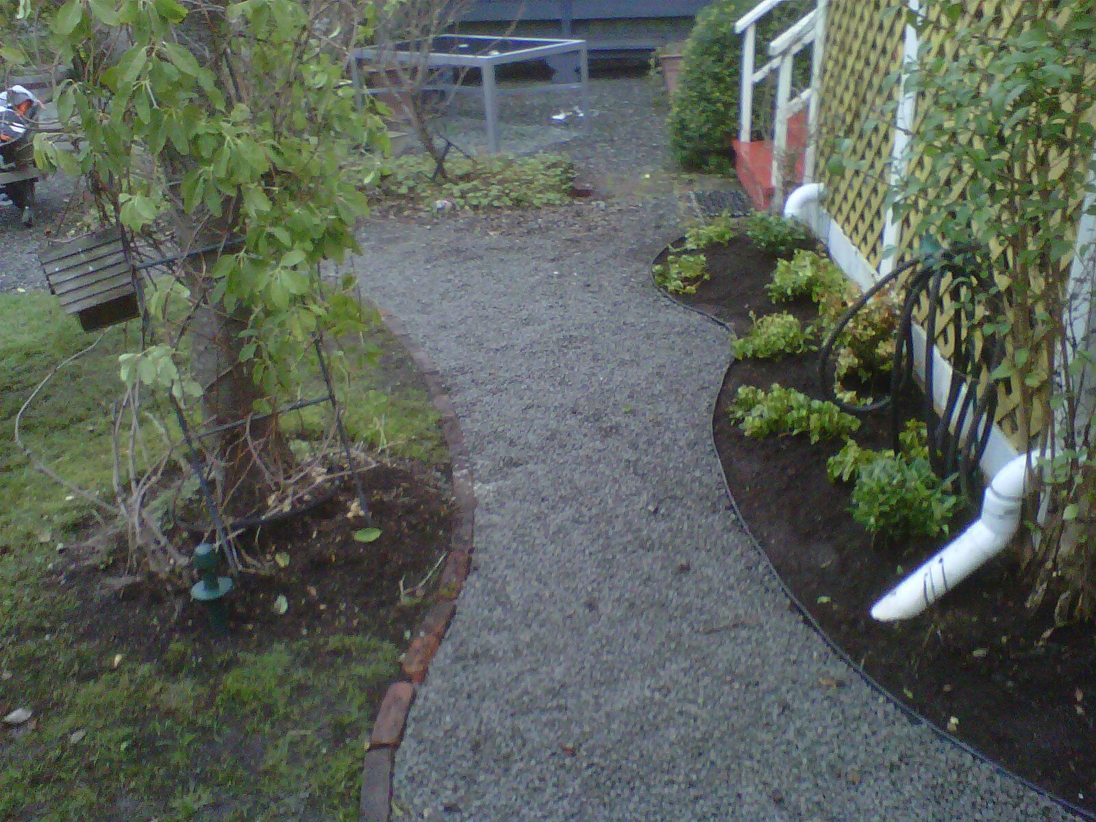 Yard storm drainage PVC pipe installed on side of walkway under flower garden