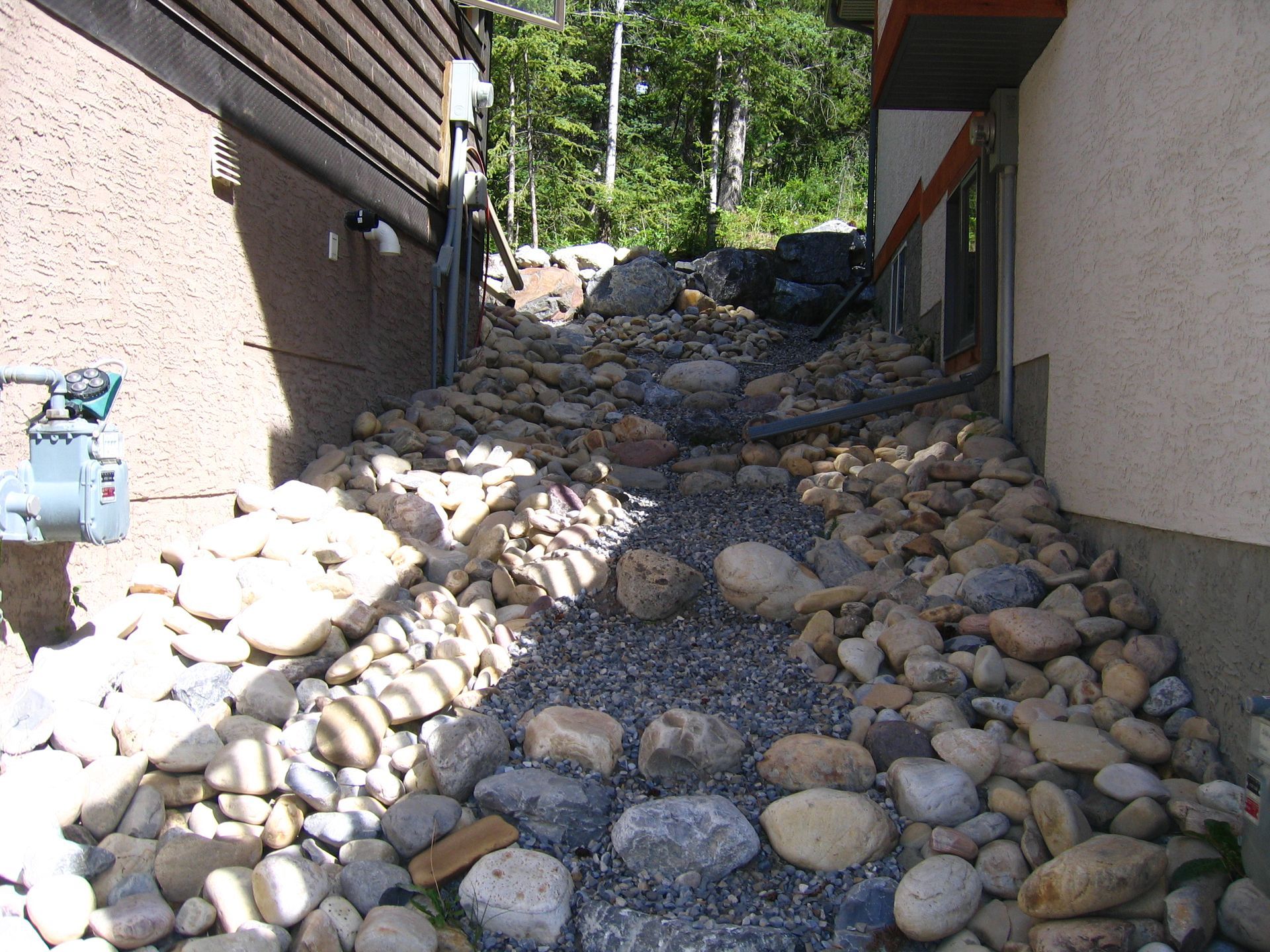 Drain rock acting as permeable surface for sloping terrain between two houses