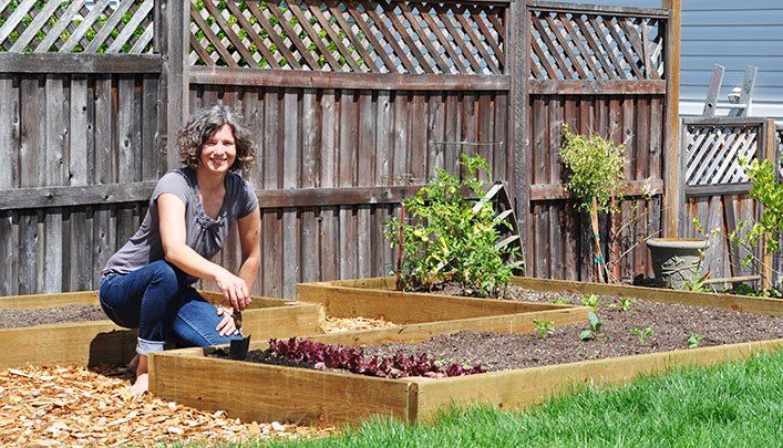RainTek customer in Crofton BC smiling at camera as she kneels by her garden bed