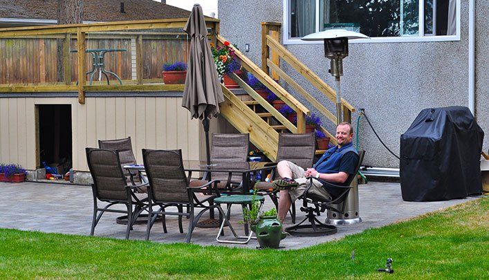 Ross Dunn a RainTek customer happy with his drainage services, sitting in a patio chair in his backyard smiling at camera