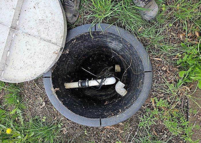 An open storm drain with the boots of a RainTek worker standing over it.