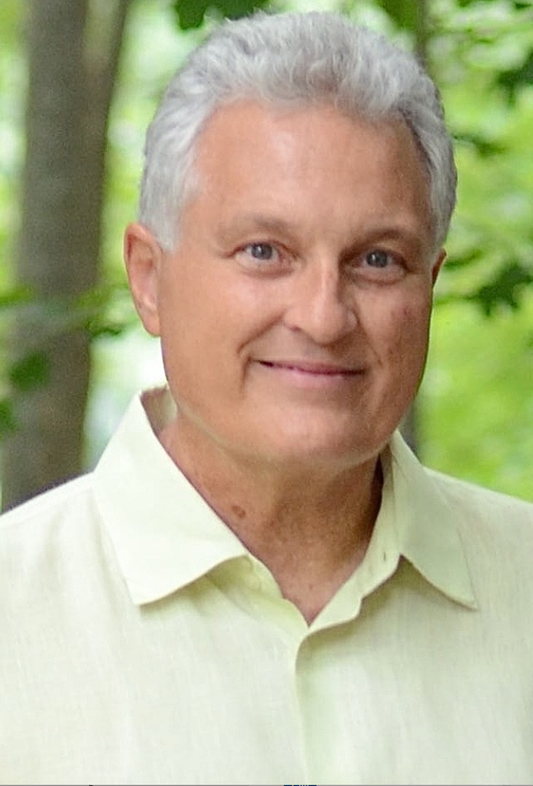A man with gray hair and a yellow shirt is smiling for the camera.